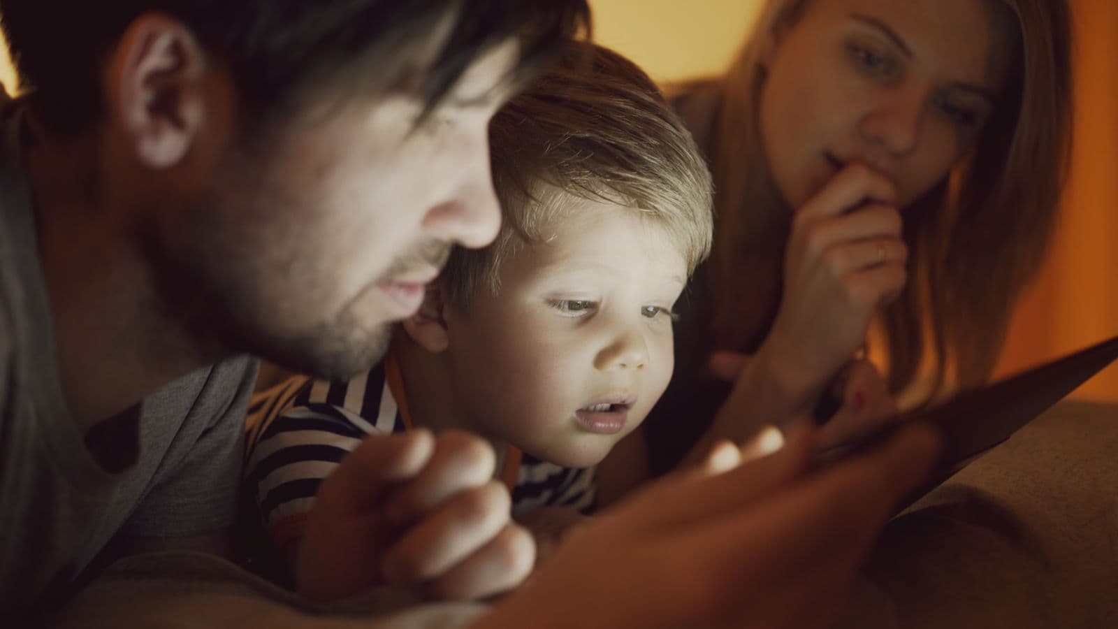 A family sitting together, warmly lit, sharing a tablet in the evening